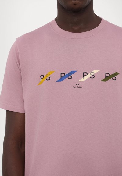 Růžové bavlněné tričko s kulatým výstřihem, na kterém je pět potištěných log "PS" v žluté, modré, béžové a zelené barvě, s jemnou texturou.