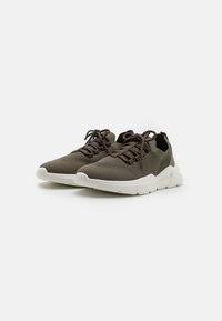 Brown knit sneakers with a textured upper, rounded toe, and white rubber sole. Features lace-up closure and soft fabric for comfort.