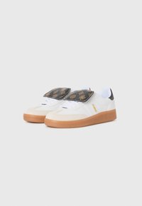 Witte sneakers met een gumrubberen zool en beige accenten. Heeft een zwarte, gestreepte klittenbandsluiting en een veterontwerp. Gemaakt van soepel leer en suède.