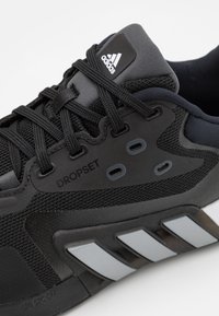 Black athletic shoe with mesh upper, reinforced overlays, and rubber sole. Features three silver stripes, branded logo, and secured lacing.