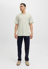 Tricou scurt cu mânecă scurtă, gri deschis, cu guler rotund, asociat cu pantaloni negri-albastri și pantofi bej. Design simplu, potrivire confortabilă.