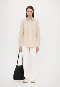 Beige stripete skjorte med knapper, løse hvite bukser og en vevd svart veske. Stoffet er glatt; skjorten har klassisk krage og mansjetter.
