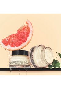 Vitaminanreichernde Gesichtsbasis in klaren Glasbehältern; einer mit einem schwarzen Deckel. Weiche Cremetextur mit einer Grapefruitscheibe darüber, aus der Saft tropft.