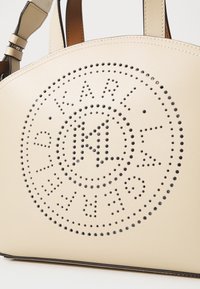 Beige leren handtas met een geperforeerd rond logo ontwerp, voorzien van contrasterende zwarte accenten en een gestructureerde silhouette.