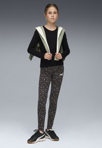 Maglietta nera a maniche lunghe, gilet verde con cappuccio, leggings neri con stampa leopardata grigia e sneakers nere con suola bianca.