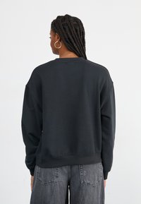 Zwarte sweatshirt met een relaxte pasvorm, ronde hals en ribgebreide manchetten. Zachte stoftextuur. Gecombineerd met grijze wijde jeans.