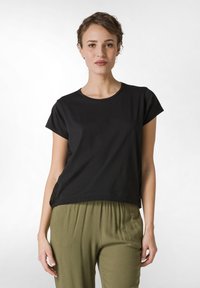 Tricou negru cu mânecă scurtă, din bumbac moale, cu decolteu rotund, asociat cu pantaloni lejeri, de culoare verde măsliniu, având o croială confortabilă.
