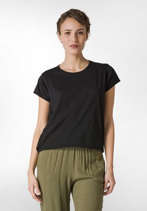 Maglietta nera a maniche corte realizzata in morbido cotone con scollatura rotonda, abbinata a pantaloni larghi verde oliva con una vestibilità comoda.