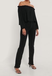Top nero fuori spalla con scollatura a volant e maniche lunghe. Abbinato a jeans neri a vita alta con orlo sfrangiato e tacchi a strap.
