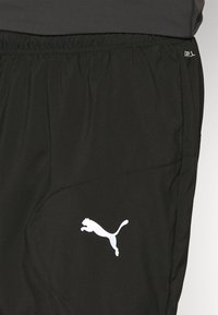 Sorte idrettsshorts laget av lett stoff, med elastisk midje, sidelomme og et reflekterende hvitt Puma-logo.
