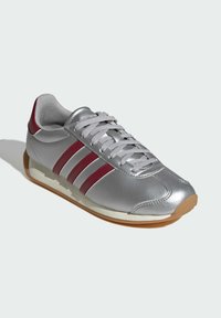 Silver synthetic sneakers with red accents, featuring three white stripes, grey laces, a rounded toe, and a gum rubber sole.