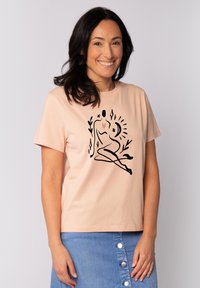 T-shirt en coton rose clair avec un design en ligne noire d'une figure assise ornée de fleurs et d'un cœur, coupe décontractée, manches courtes.