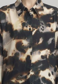 Camicia a maniche corte realizzata in tessuto leggero, caratterizzata da un mix di motivi astratti in nero, marrone e beige; presenta un colletto a punta e bottoni.