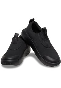 Svarta slip-on skor tillverkade av ventilerande meshmaterial, med en texturerad ovandel, gummisula och dragflik för enkelt påtagande.