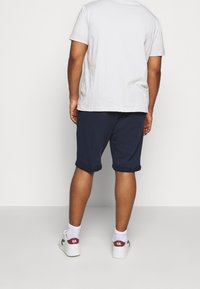 Mörkblå bomullsshorts med upprullade fållar, tillsammans med en ljusgrå kortärmad skjorta och vita sneakers med detaljer.