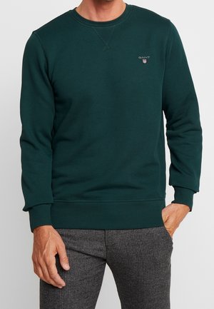 Sweatshirt vert foncé en coton doux, avec col rond, poignets et ourlet côtelés, et un petit logo sur la poitrine.