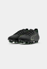 Une paire de crampons de football noirs avec des pointes vertes et des détails de logo vert subtil sur fond blanc.
