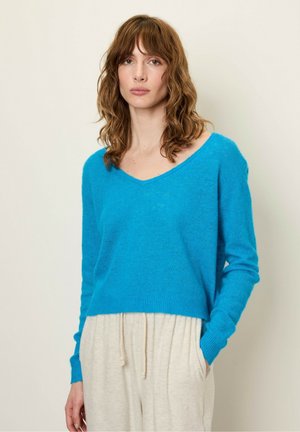 Pull bleu à col en V avec des manches longues, fabriqué à partir d'un tissu doux et texturé. Son design court complète des pantalons légers à coupe décontractée.