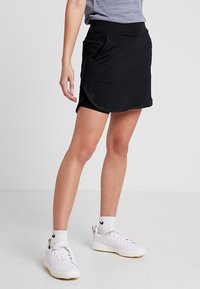 Černá sportovní sukně s elastickým pasem, bočními kapsami a zakřiveným lemem. Vyrobena z lehké a pružné tkaniny, vhodná pro aktivní nošení.