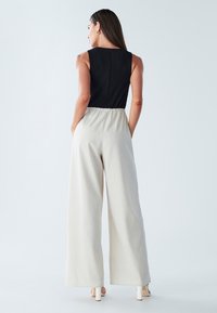 Melns smoksēts korsete, kombinēts ar gaiši bēšām platām biksēm. Apģērbs ir ar brīvu piegriezumu un elastīgu jostasvietu. Sandales ar bloka papēdi.