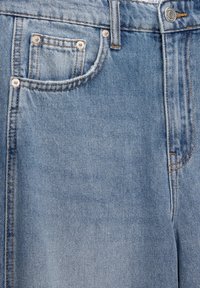 Světlé modré džíny z denimu s vyšisovanou texturou, malou přední kapsou a žlutým prošíváním. Obsahují kovové zapínání na knoflík a nýtování.