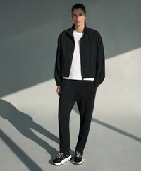 Čierna ľahká bomber bunda s stojacím golierom, pod ňou biele tričko, voľné čierne nohavice a čierno-biele tenisky.