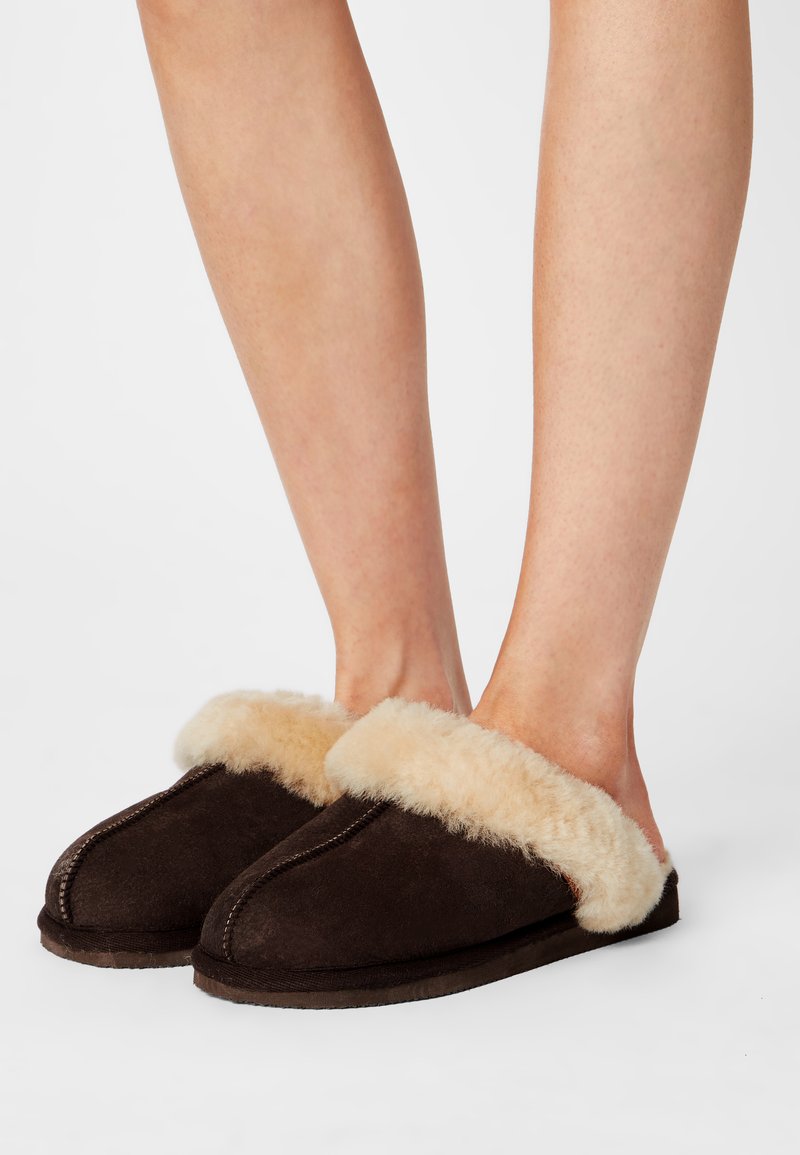 Brune semskede tøfler med en fluffy beige faux fur krave. Designet er åbent foran med flad sål og synlige sømdetaljer.