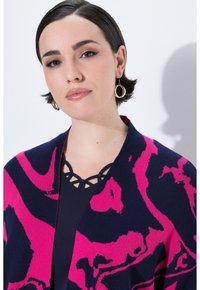 Pestrý šál v námořnické modři a fuchsiové barvě s abstraktním vzorem, zkombinovaný s tmavým topem a černým geometrickým náhrdelníkem. Kroužkové zlaté náušnice.