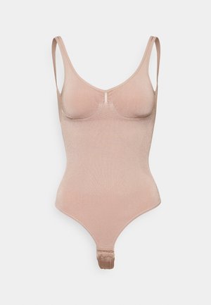 Nude bodysuit with thin straps, seamless design, and a textured bust area. Features a thong back and snap closure at the bottom.
