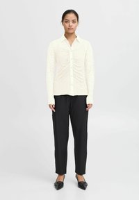 Cremfarbens Langarmhemd mit strukturiertem Muster, kombiniert mit schwarzen tapered Jeans und spitzen schwarzen Ballerinas. Minimalistisches Design.