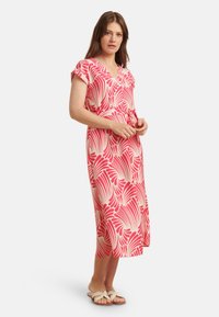 Rosa Midi-Kleid mit V-Ausschnitt und kurzen Ärmeln, mit einem weißen Blattmuster. Die Taille ist mit einem passenden Band gerafft.