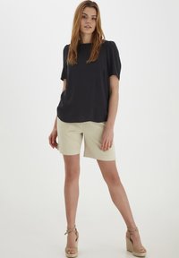 Top nero a maniche corte con scollatura tonda, abbinato a pantaloni corti beige lungo ginocchio e sandali con zeppa in espadrille color testa di moro. Design semplice, texture liscia.