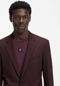 Weinroter Blazer mit schmaler Passform, Reverskragen und einreihiger Knopfleiste, getragen über einem passenden weinroten Rundhalsausschnitt-Shirt.