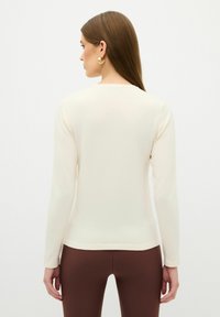 Langärmliges, eng anliegendes Oberteil aus cremefarbenem Rippstrick, mit einem runden Ausschnitt und nahtloser Verarbeitung, kombiniert mit braunen, hoch geschnittenen Leggings.