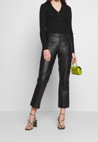 Top nero a coste con maniche lunghe e bottoni, abbinato a pantaloni cropped in pelle nera a vita alta e una mini borsa verde. Tacchi verde con cinturini.