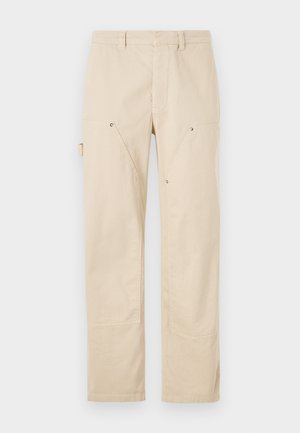 Beige cargo pants made from a textured fabric, featuring pockets with angled flaps and metal snap fasteners. Straight leg design.