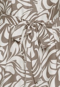 Hnedo-biele šaty s tropickým listovým vzorom a látkovým opaskom previazaným na mašľu v páse.