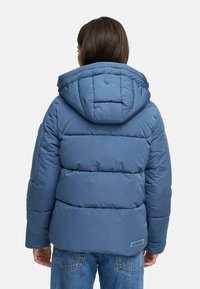 Blå pufferjacka med huva, med kviltade sektioner och elastiska cuffar. Bakdelen har en liten logotyp och en avslappnad passform.