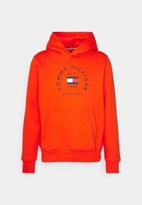 Fel oranje capuchontrui met een voorkantzak. Heeft een rond logo met de tekst "TOMMY HILFIGER EST. 1985" en een vlagontwerp.