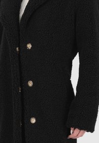 Cappotto di pile nero con finitura testurizzata, dotato di colletto a scialle e quattro grandi bottoni chiari sul davanti.