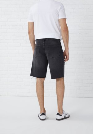 Pantalones cortos de mezclilla negros con dobladillo deshilachado, que cuentan con cinco bolsillos y un corte clásico, combinados con una camiseta blanca sencilla y zapatillas negras.