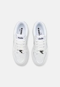 Sneaker in pelle bianca con perforazioni sulla punta, lacci piatti e un accento di logo nero. Superficie liscia con un design atletico classico.