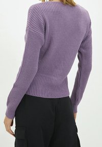Paarse gebreide trui met een gestructureerde afwerking, lange mouwen en een getailleerde taille. Draagt over zwarte cargobroek, wat een casual stijl laat zien.