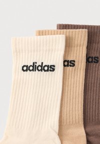 Kolm ribidega sokipaari heledas beežis, keskmises beežis ja pruunis, mille kõigi sokkide peal on must adidas logo.