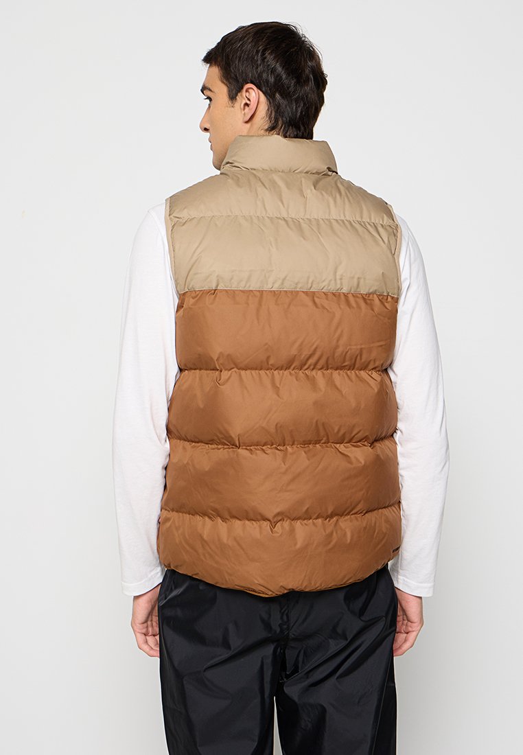 Gilet rembourré avec une partie supérieure beige et une partie inférieure marron. Design matelassé avec un col haut. Matériau en nylon léger.