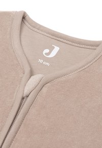 Beige fleece kledingstuk met een gladde textuur, ronde halslijn en ritssluiting. Etiket toont maat "70 cm" en een gestileerde "J."