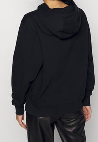 Czarna bluza z kapturem wykonana z miękkiego materiału o luźnym kroju, z prążkowanymi mankietami i dołem oraz gładką fakturą.