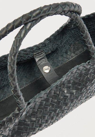 Μαύρη υφασμένη δερμάτινη τσάντα χειρός με πλεκτές λαβές και κλείσιμο με δερμάτινο λουράκι με κουμπί, απεικονιζόμενη από μια λοξή κορυφαία γωνία.