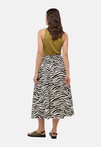 Débardeur côtelé vert olive associé à une jupe longue avec un motif rayé zèbre noir et blanc et une taille froncée. Sandales décontractées.