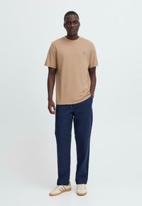 Brun bomull t-skjorte med rund hals og korte ermer, sammen med marineblå bukser. Utseendet fullføres med beige joggesko med striper.